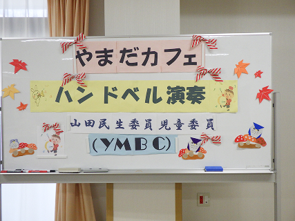 やまだカフェ ハンドベル演奏 山田民生委員児童委員 （YMBC）と書かれた紙がホワイトボードに貼り付けられています。