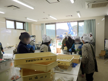 餅がばんじゅうに入れられており、白い三角巾を付けた女性たちが作業を行っています。