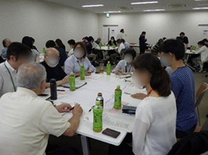 ご年配の方々が４、５人ずつに分かれてテーブルに座っており、各テーブルでグループごとの話し合いが行われています。